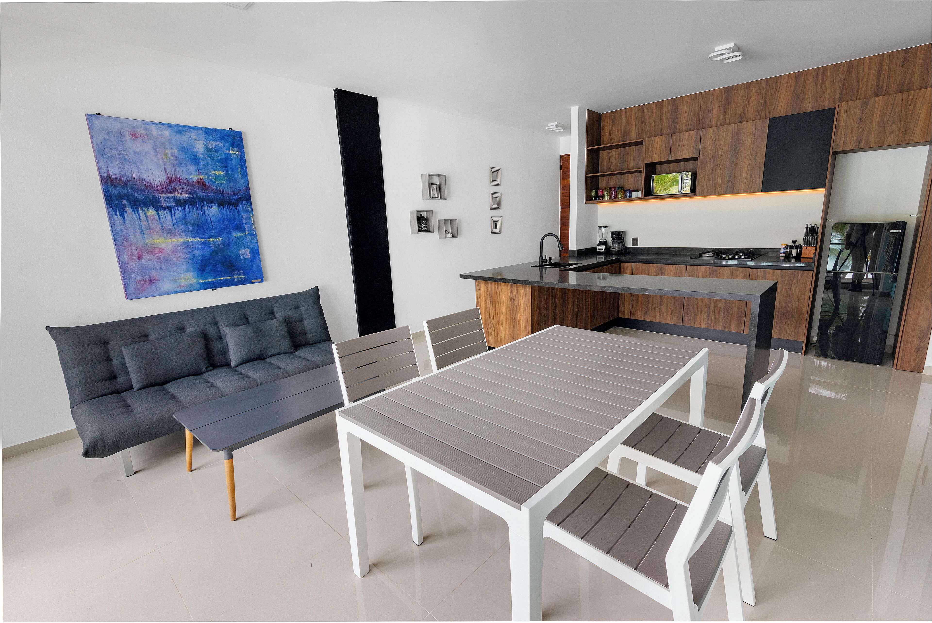 Une cuisine moderne avec un îlot central, un coin repas avec une table et des chaises, et un canapé gris.