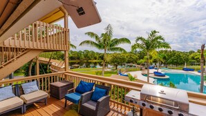 A deck with outdoor furniture, a grill, and a view of a swimming pool and palm trees. - Unique Home Resort W/ Coolest Amenities and Games! (Jensen Beach)