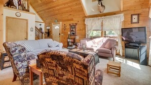 A cozy log cabin interior with a loft bedroom, a fireplace, a television, and a bookshelf. - Virginia Mountain Cabin w/ Decks & Fireplaces (Fulks Run)