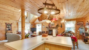 A cozy cabin interior with a wooden ceiling, a central island with a sink, a dining area with a red tablecloth, and a fireplace with a Christmas tree. - Virginia Mountain Cabin w/ Decks & Fireplaces (Fulks Run)