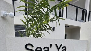 A sign with the name 'Sea'Ya' on a textured wall, surrounded by greenery and a modern building in the background. - Brand New- Modern Sea' Ya Villa (Fitts Village)