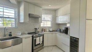 A modern kitchen with white cabinets, stainless steel appliances, and a window providing natural light. - Brand New- Modern Sea' Ya Villa (Fitts Village)