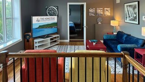 A modern living room with a television, a blue sofa, and a wooden staircase. - Captain's suite @ The Homestead Oceanfront (Norman's Cove-Long Cove)