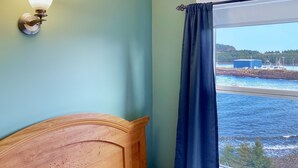 Una habitación con cabecera de madera, una lámpara de pared y una ventana con vista a un puerto y barcos.