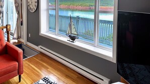 A room with a large window overlooking a lake, a sailboat model, and a clock on the wall.