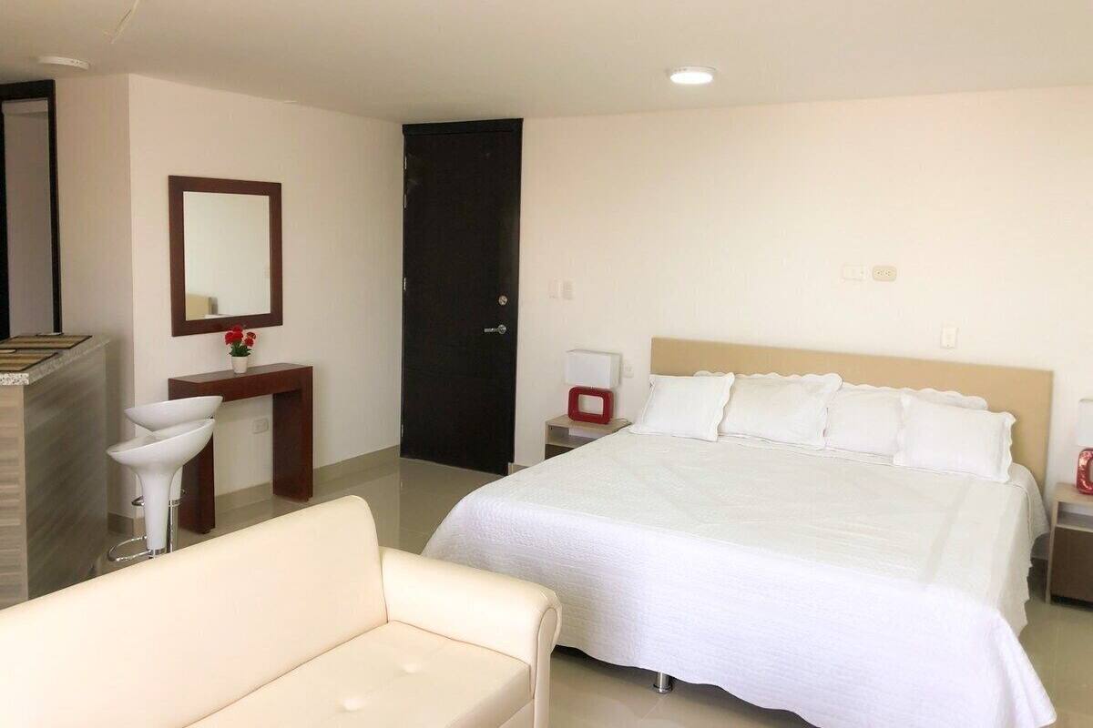 A hotel room with a bed, a bedside table, a chair, a desk, a mirror, and a door.