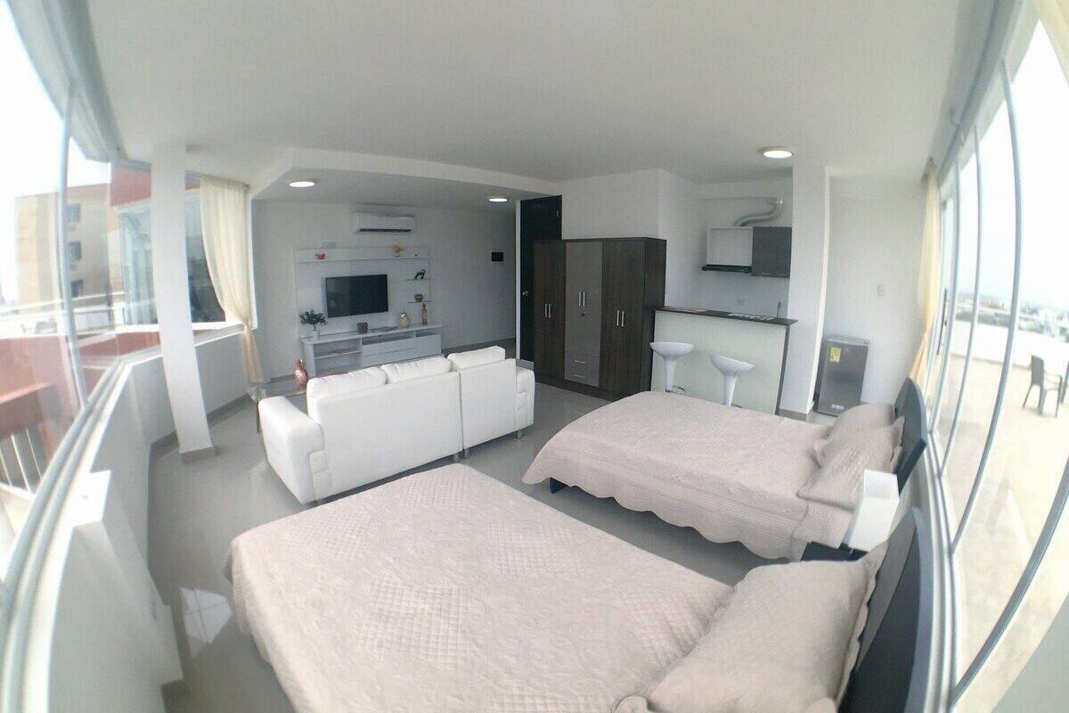 A modern hotel room with two beds, a sofa, a kitchenette, and a balcony with a view.