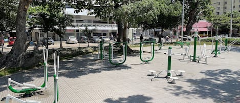 Outdoor exercise equipment in a public park area with trees and a building in the background.