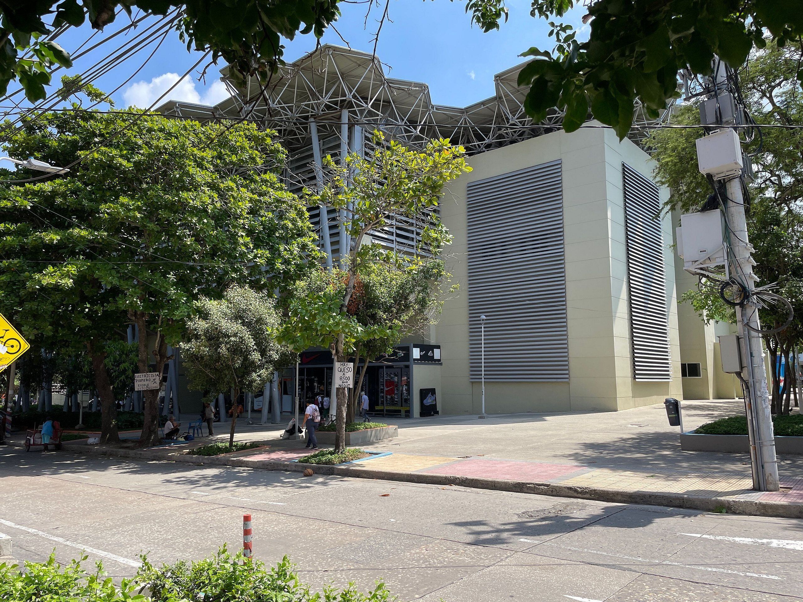Vista de la calle con un edificio que destaca por su amplia fachada moderna con listones horizontales y una acera bordeada de árboles.