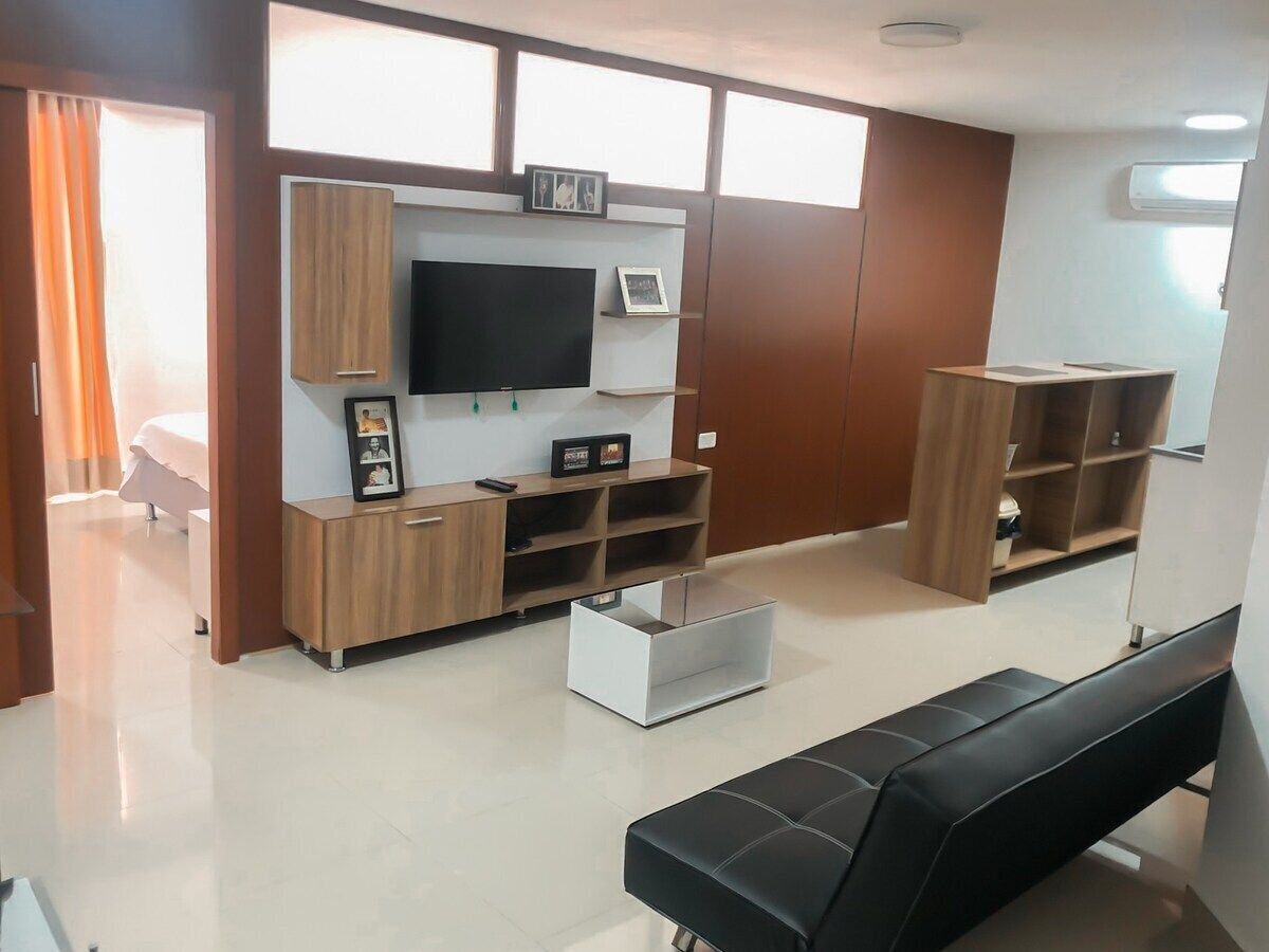 A modern living room with a flat-screen TV, wooden cabinets, a white coffee table, and a black sofa.