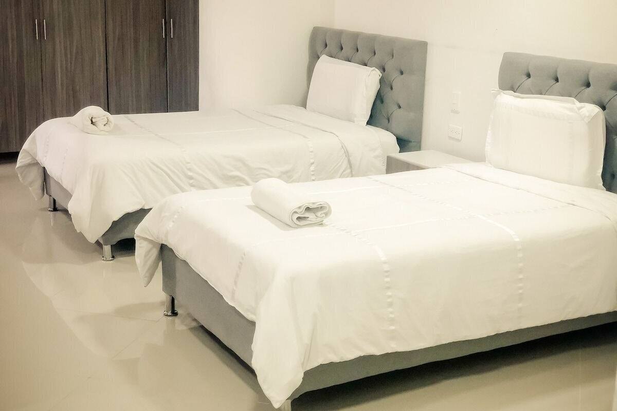 Two single beds with grey headboards and white bedding in a hotel room.