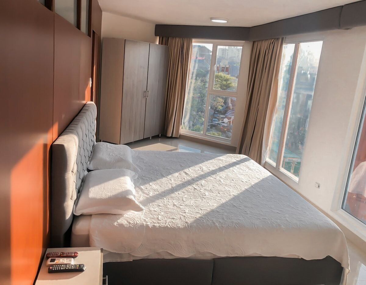 Een moderne hotelkamer met een groot bed, een kledingkast en uitzicht op de stad door grote ramen.