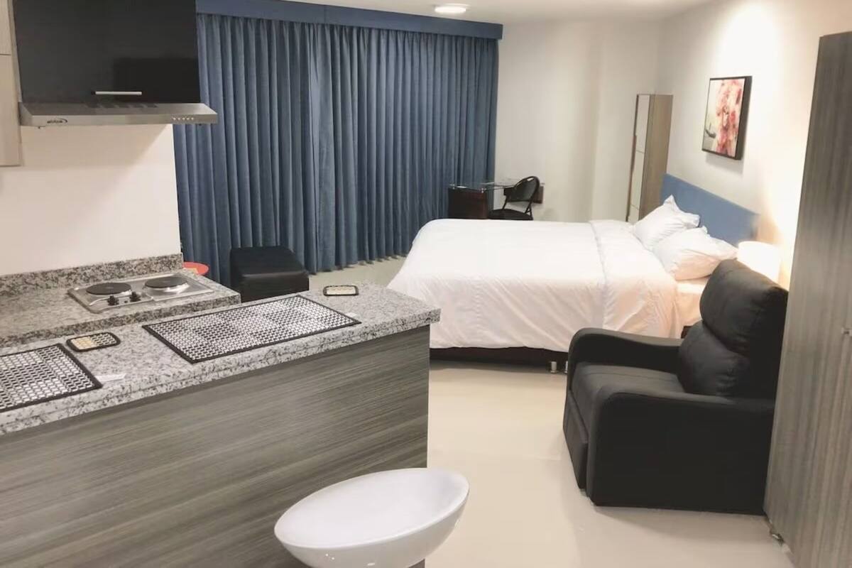 A hotel room with a bed, a desk with a chair, a small table, a sofa, and a TV.