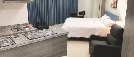 Habitación de hotel con cama, escritorio con silla, una mesita, sofá y televisor.