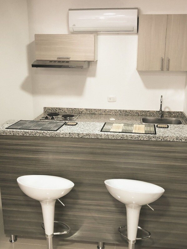 A kitchen with a granite countertop, a gas stove, a sink, and two white bar stools.
