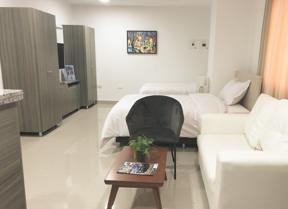 Una habitación de hotel moderna con cama, sofá, una mesita con una revista, una silla y un cuadro en la pared.