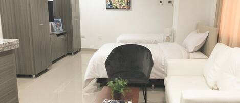 Una habitación de hotel moderna con cama, sofá, una mesita con una revista, una silla y un cuadro en la pared.