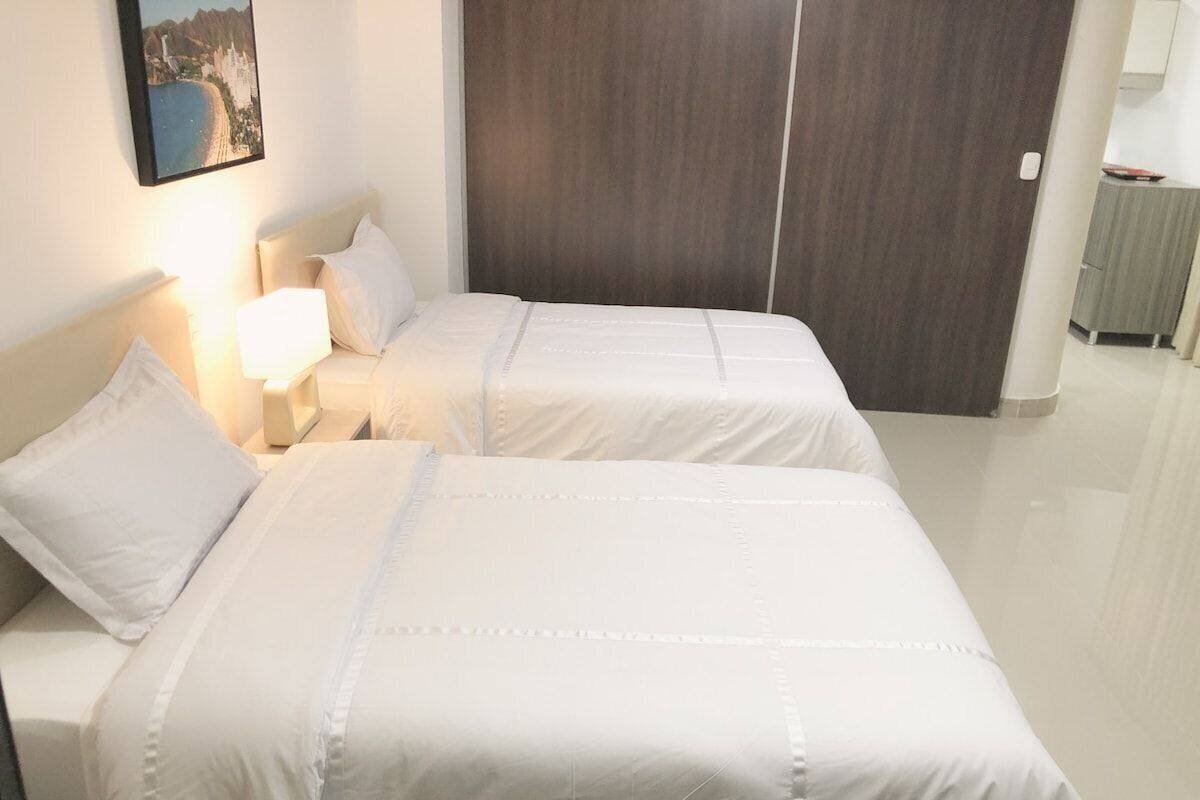 A hotel room with two beds, a nightstand, a lamp, and a framed picture on the wall.