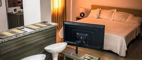 A hotel room with a bed, bedside table, lamp, and a small seating area with stools.
