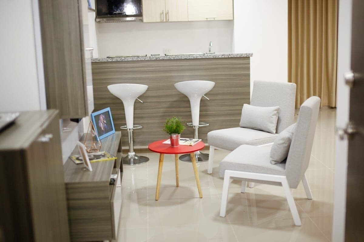A modern kitchen with a wooden countertop, a built-in stove, and a sink. There is a dining area with a white chair and a small red table with a plant.