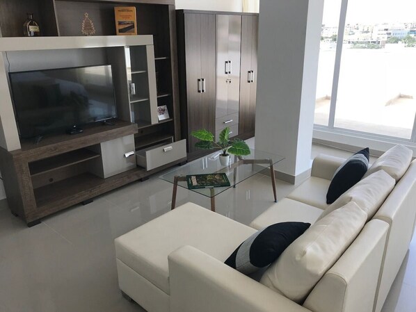 Una sala de estar moderna con un televisor de pantalla plana, un sofá, una mesa de centro de vidrio y un aparador con cajones.
