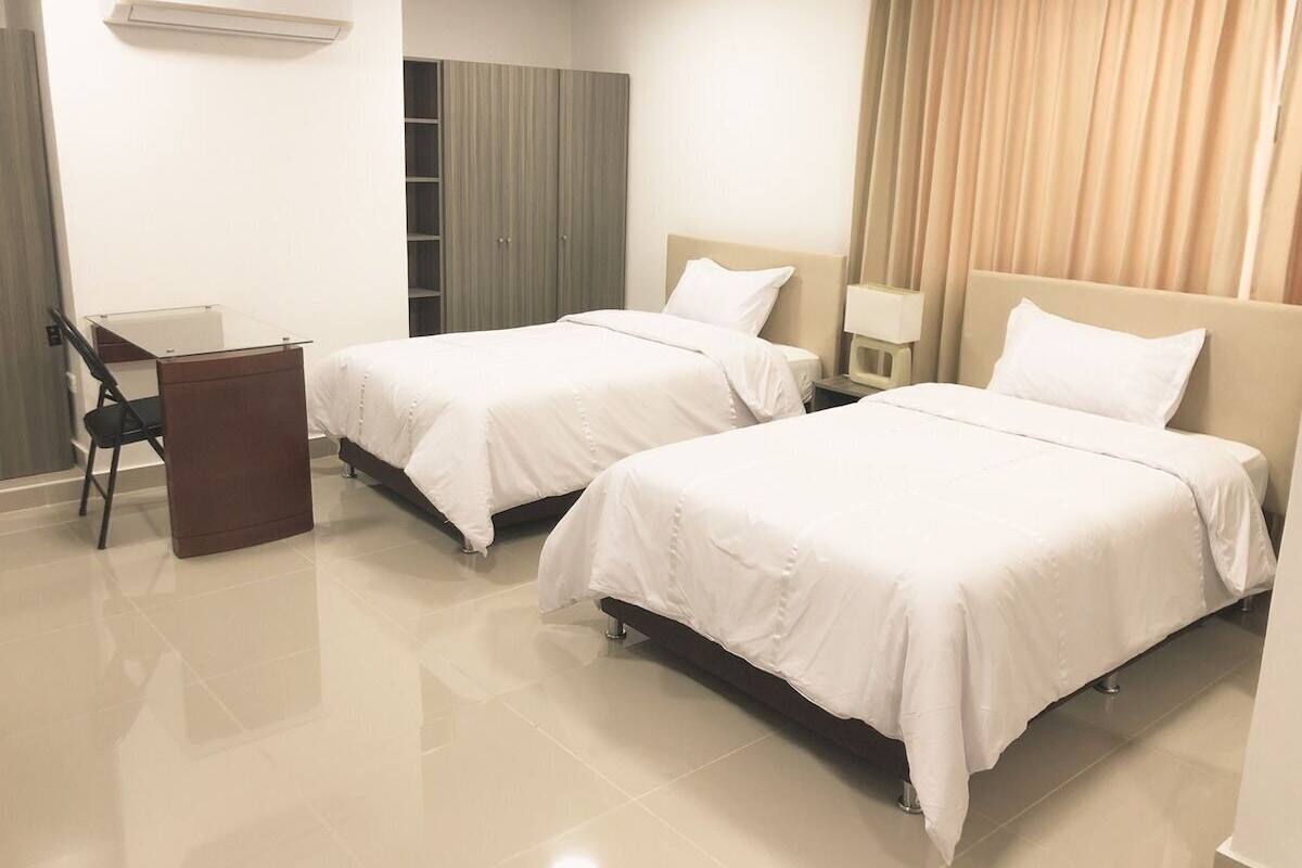 A hotel room with two beds, a desk, a chair, and a wardrobe.