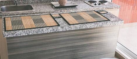 Cocina compacta con encimera de granito, estufa integrada, pileta y dos taburetes blancos.