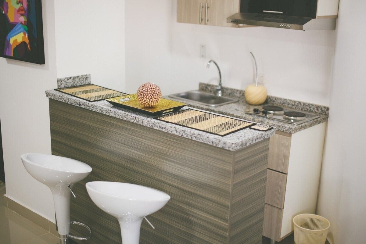 A modern kitchen with a granite countertop, two white bar stools, a sink, and a stove.