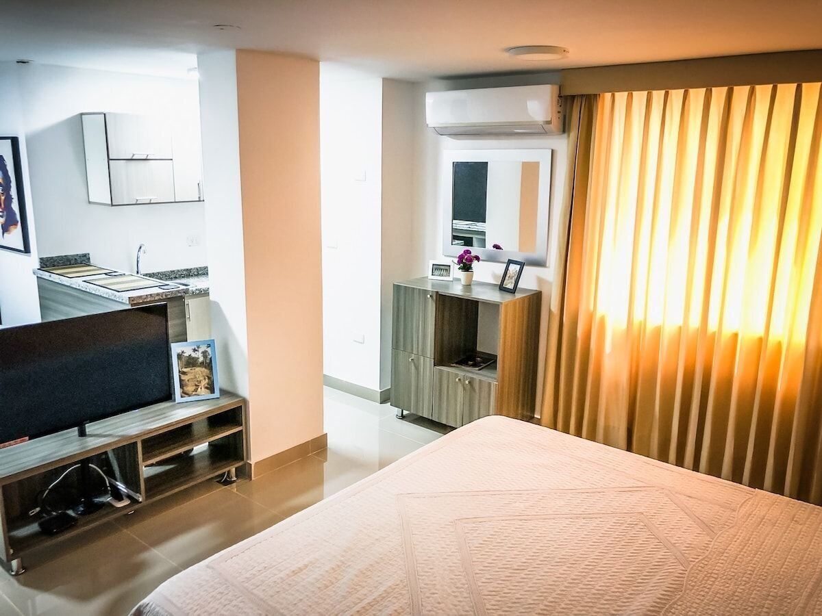 A hotel room with a bed, a TV, a small kitchenette, and a bathroom.
