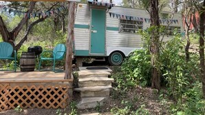 Un espacio al aire libre rústico con una caravana antigua, una terraza de madera y un letrero de bienvenida.
