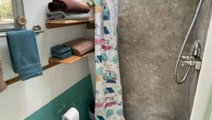 Un baño compacto con ducha, inodoro y un estante pequeño con toallas.