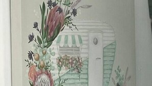 Una habitación con un cuadro floral en la pared, una puerta a rayas verdes y una mesita con un objeto decorativo.