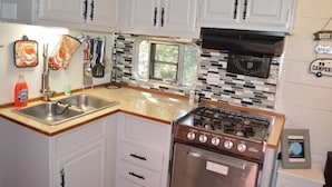 A compact kitchen with white cabinets, a stainless steel sink, a gas stove, and a small window. - The Blue Moon on Hamilton Creek (Burnet County)