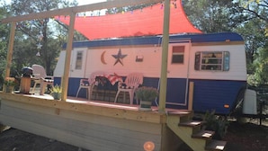 A mobile home with a star and crescent design, a porch with chairs, and a red canopy. - The Blue Moon on Hamilton Creek (Burnet County)