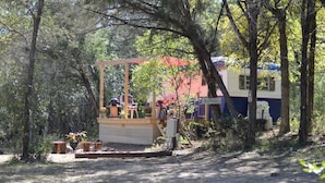 A rustic wooden structure with a bench and a table, surrounded by trees and a parked RV. - The Blue Moon on Hamilton Creek (Burnet County)