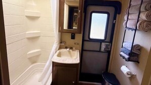 A compact bathroom with a bathtub, sink, mirror, toilet, and towel rack.