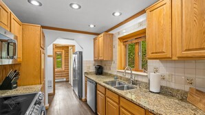 A kitchen with wooden cabinets, granite countertops, stainless steel appliances, and a window with a view of greenery. - Cabin near Bridger Bowl with Hot Tub!  (Bozeman)