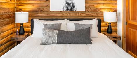 A wooden log cabin-style bedroom with a bed, two bedside tables, lamps, and a framed picture of a bull.
