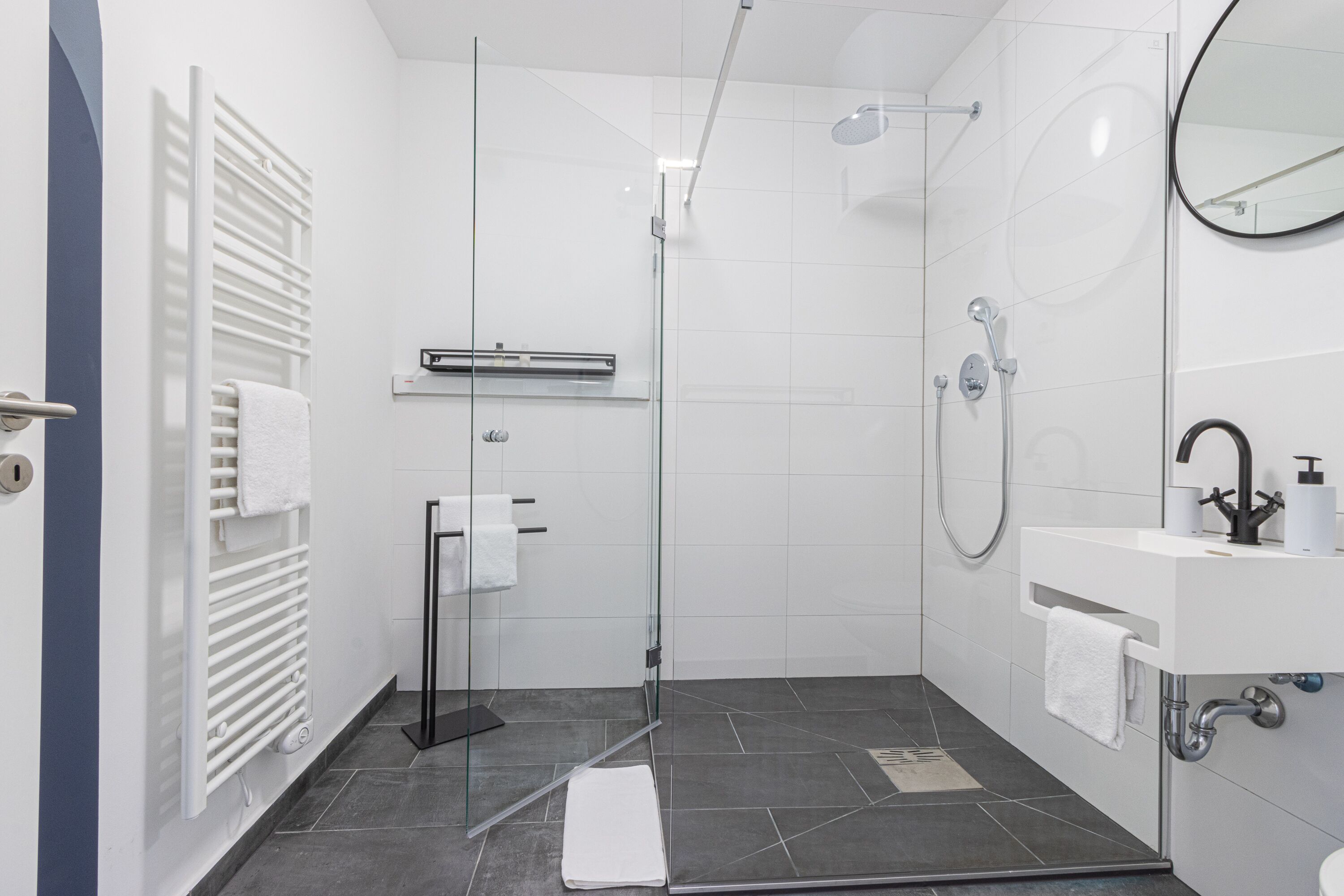 A modern bathroom with a glass shower enclosure, a white sink with a mirror, and a towel rack.