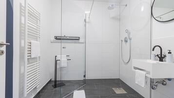 A modern bathroom with a glass shower enclosure, a white sink with a mirror, and a towel rack.