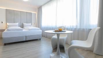 Una camera d'albergo moderna con un letto, un tavolino rotondo con una ciotola di frutta e una sedia bianca.