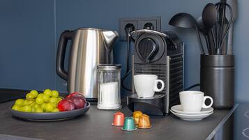 A kitchen counter with a coffee maker, a kettle, a bowl of fruit, and a coffee cup.