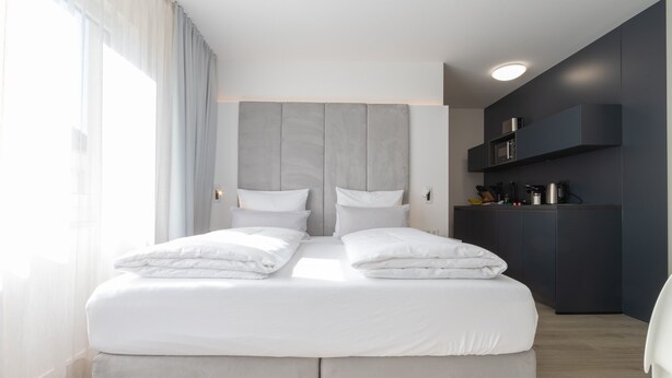 A modern hotel room with a large bed, a built-in wardrobe, and a kitchenette area. - zzzpace Smart-Hotel Bielefeld (Bielefeld)