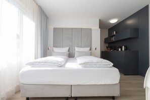 A modern hotel room with a large bed, a built-in wardrobe, and a kitchenette area. - zzzpace Smart-Hotel Bielefeld (Bielefeld)