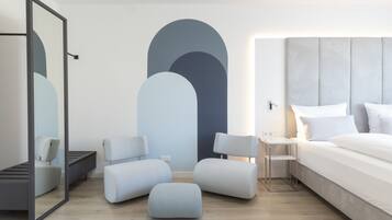 A modern bedroom with a bed, bedside tables, a mirror, and a seating area with ottomans.