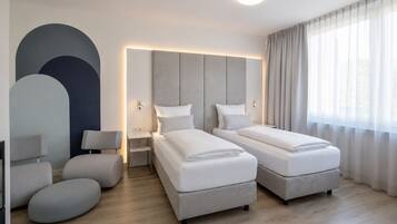 Una habitación de hotel moderna con dos camas, una mesita de noche, una lámpara y un ventanal grande con cortinas.
