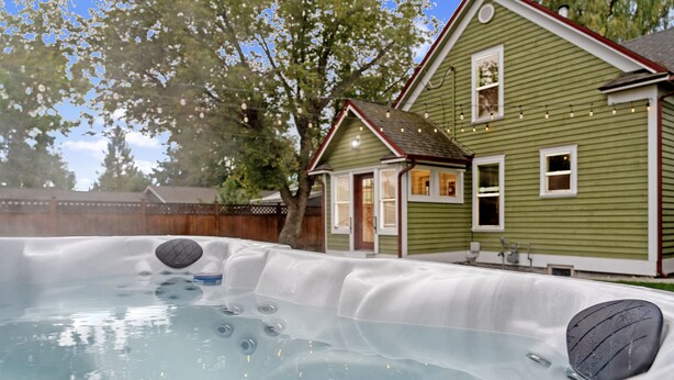 Ein Whirlpool mit mehreren Düsen, eine Holzterrasse und ein Haus mit grüner Fassade und weißen Verzierungen.