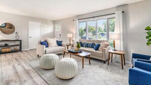 Ein modernes Wohnzimmer mit einer Sofagarnitur, Poufs, einem Couchtisch und einem Beistelltisch.