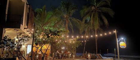 Propiedad frente a la playa con zona de comedor, palmeras y un letrero que indica un restaurante.