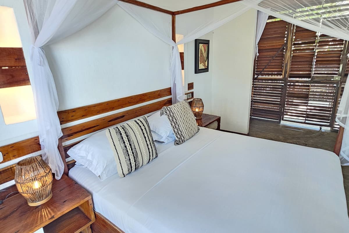 A large bed with a canopy, wooden headboard, and white bedding. There is a bedside table with a lamp and a decorative item.